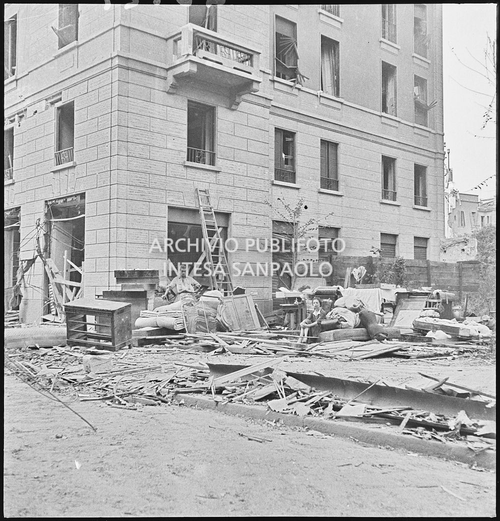 In una via di Milano  una donna siede su un materasso per strada vicino alle masserizie, recuperate dalle abitazioni bombardate, in mezzo alle macerie