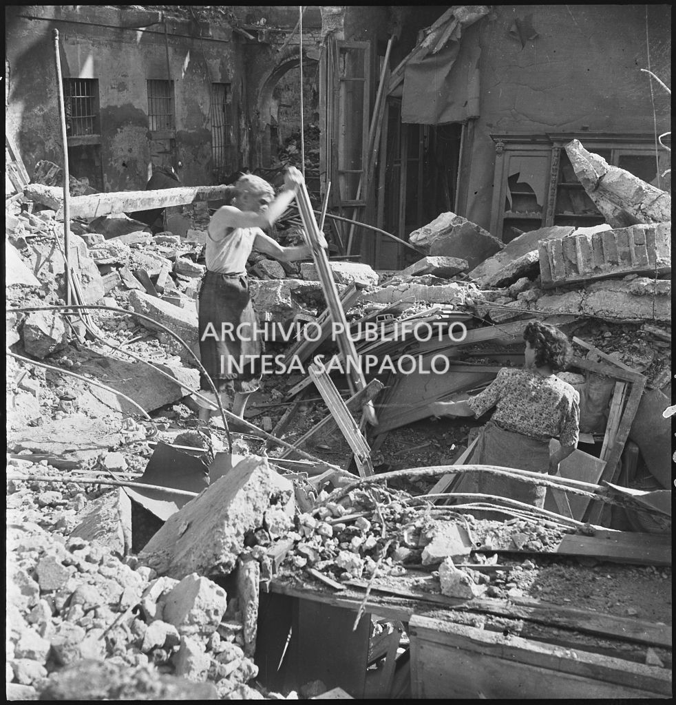 Un uomo e una donna tra le macerie degli edifici distrutti dai bombardamenti in via Beno de' Gozzadini (via che oggi non esiste più, collegava corso Italia all'allora corso Roma, oggi corso di Porta Romana)