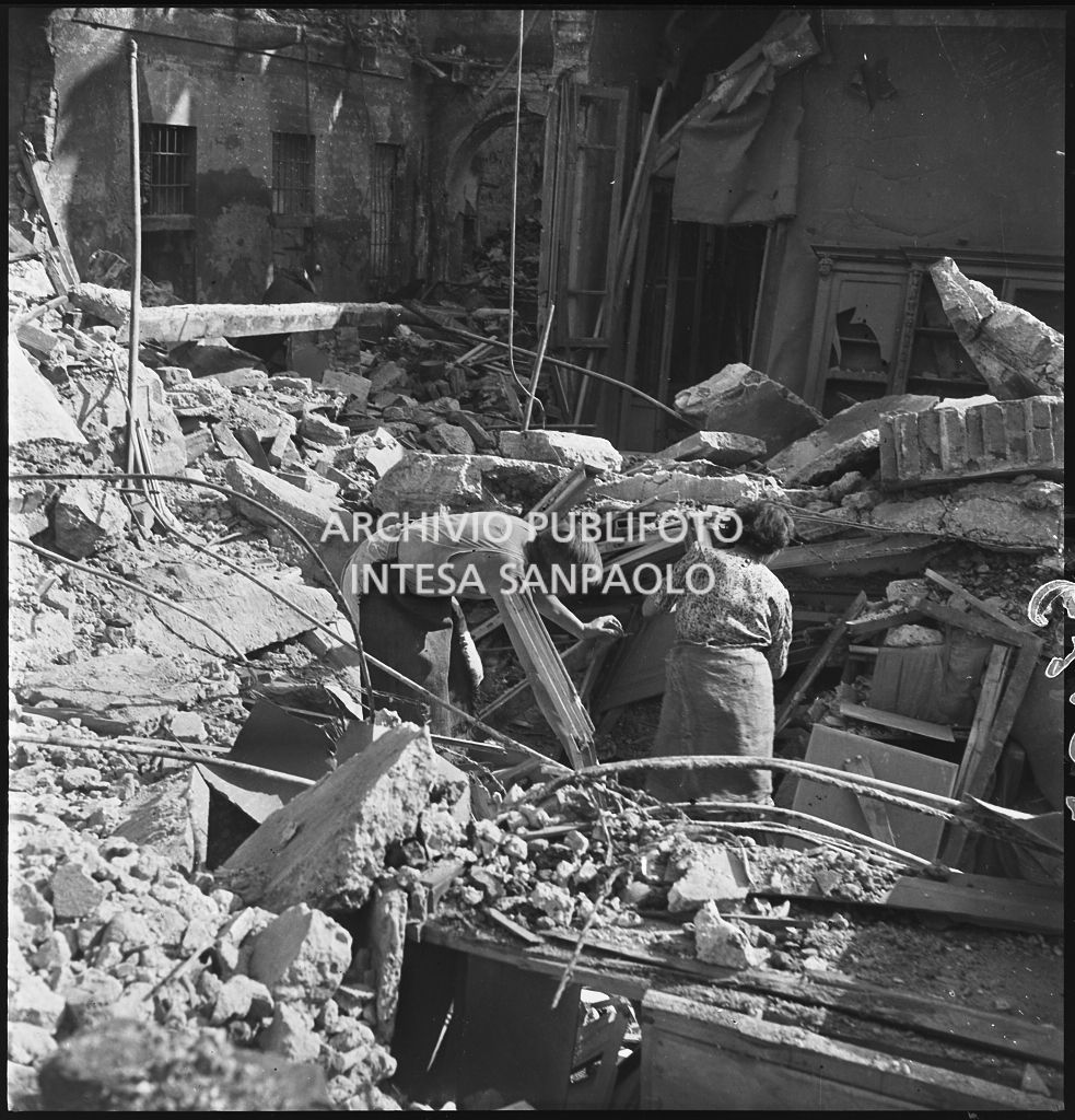 Un uomo e una donna tra le macerie degli edifici distrutti dai bombardamenti in via Beno de' Gozzadini (via che oggi non esiste più, collegava corso Italia all'allora corso Roma, oggi corso di Porta Romana)