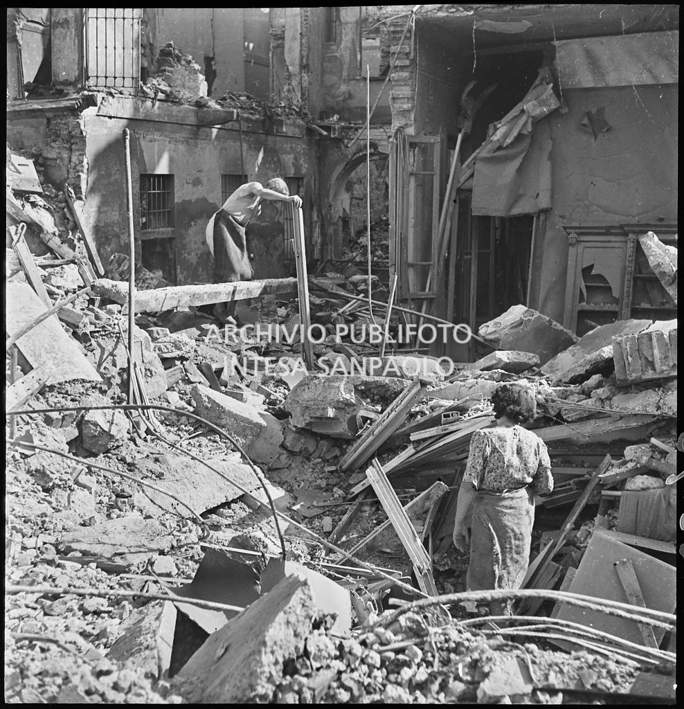 Un uomo e una donna tra le macerie degli edifici distrutti dai bombardamenti in via Beno de' Gozzadini  (via che oggi non esiste più, collegava corso Italia all'allora corso Roma, oggi corso di Porta Romana)