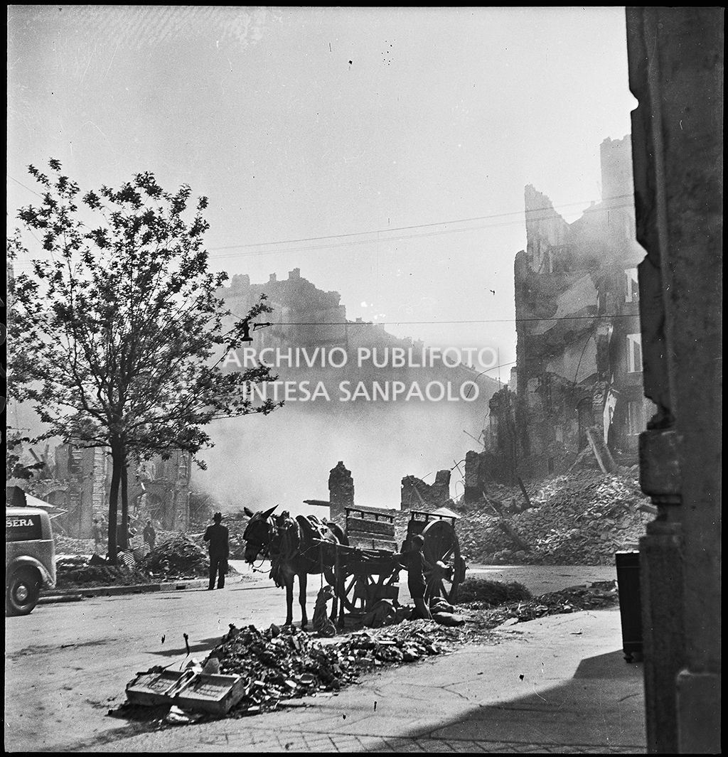 Un ragazzino, fermo a fianco a un carretto trainato da un cavallo, in via Lecco a Milano all'indomani dei bombardamenti che hanno distrutto gli edifici della via e la cui polvere è ancora nell'aria