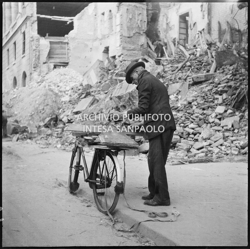 Un uomo carica sul portapacchi della sua bicicletta pezzi di legno recuperati tra le macerie degli edifici bombardati a Milano