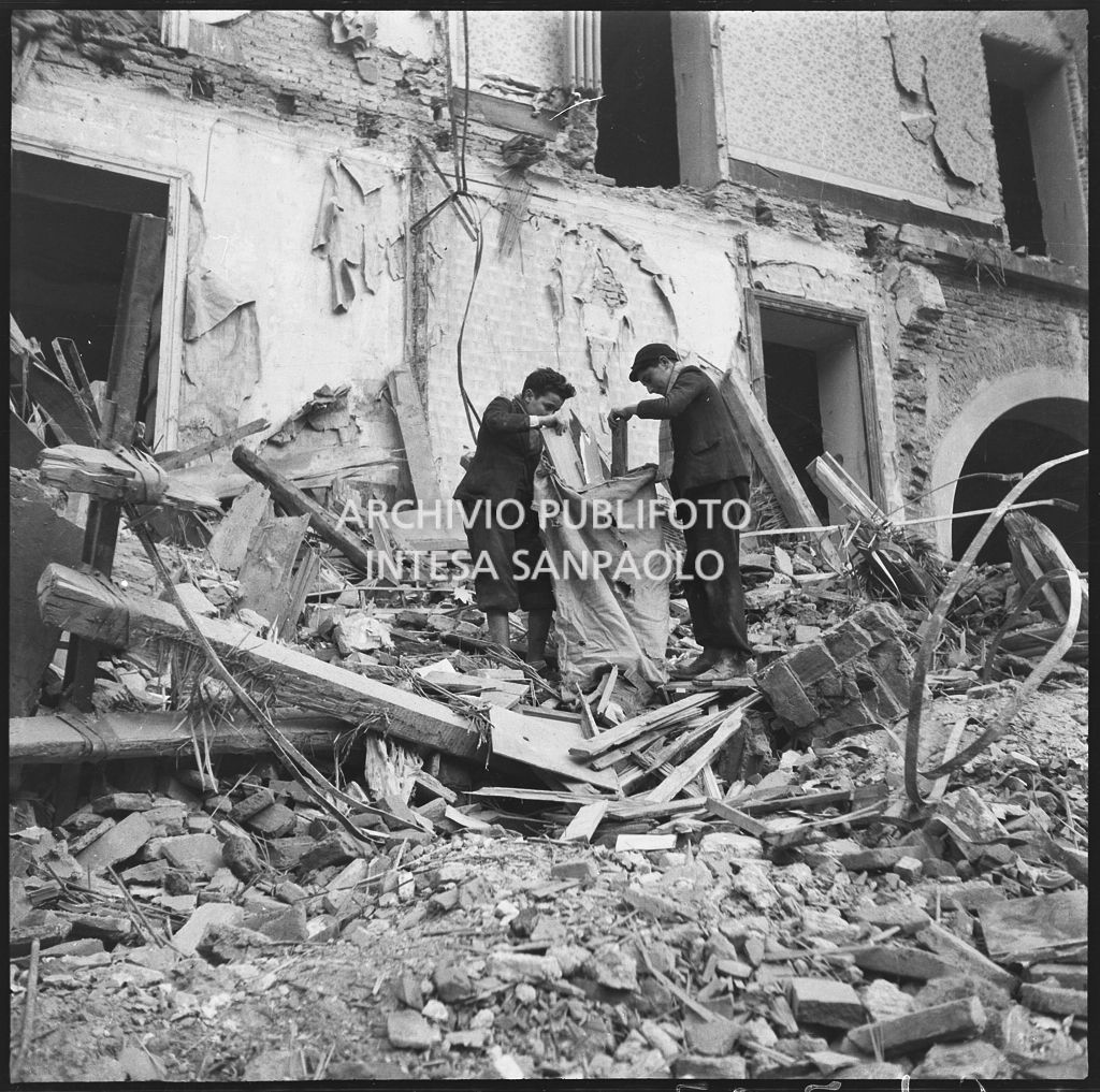 Due ragazzi raccolgono in un sacco alcuni pezzi di legno recuperati tra le macerie degli edifici bombardati a Milano