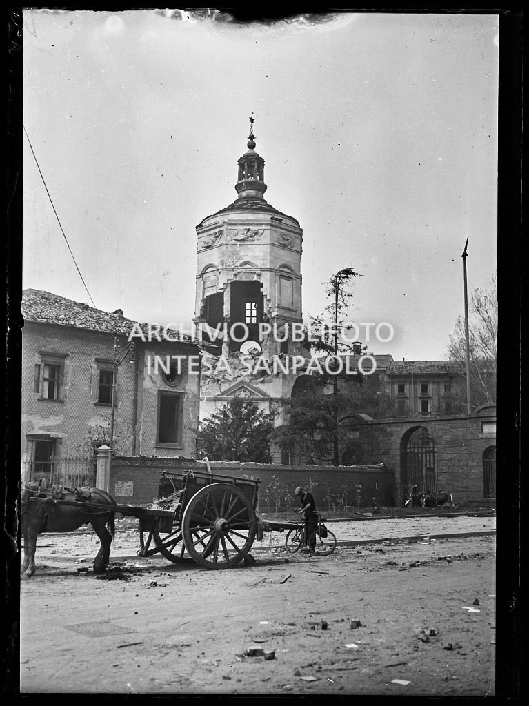 Il Monumento ai caduti, in piazza Sant'Amborgio, sventrato dai bombardamenti. In primo piano un carretto attaccato a un cavallo e un uomo in bicicletta