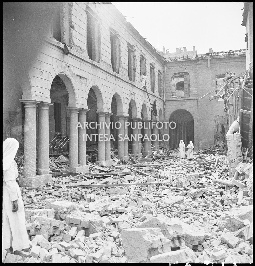 Un cortile dell'Ospedale San Giuseppe ingombro delle macerie dei bombardamenti che lo hanno gravemente danneggiato; sullo sfondo due religiose