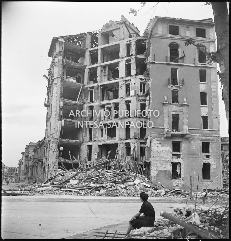 Una donna seduta in via Giovanni Pascoli guarda gli edifici sventrati dai bombardamenti