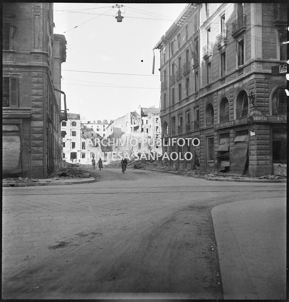 Viale Papiniano con gli edifici bombardati e le macerie addossate ai lati della strada. A destra una tabaccheria