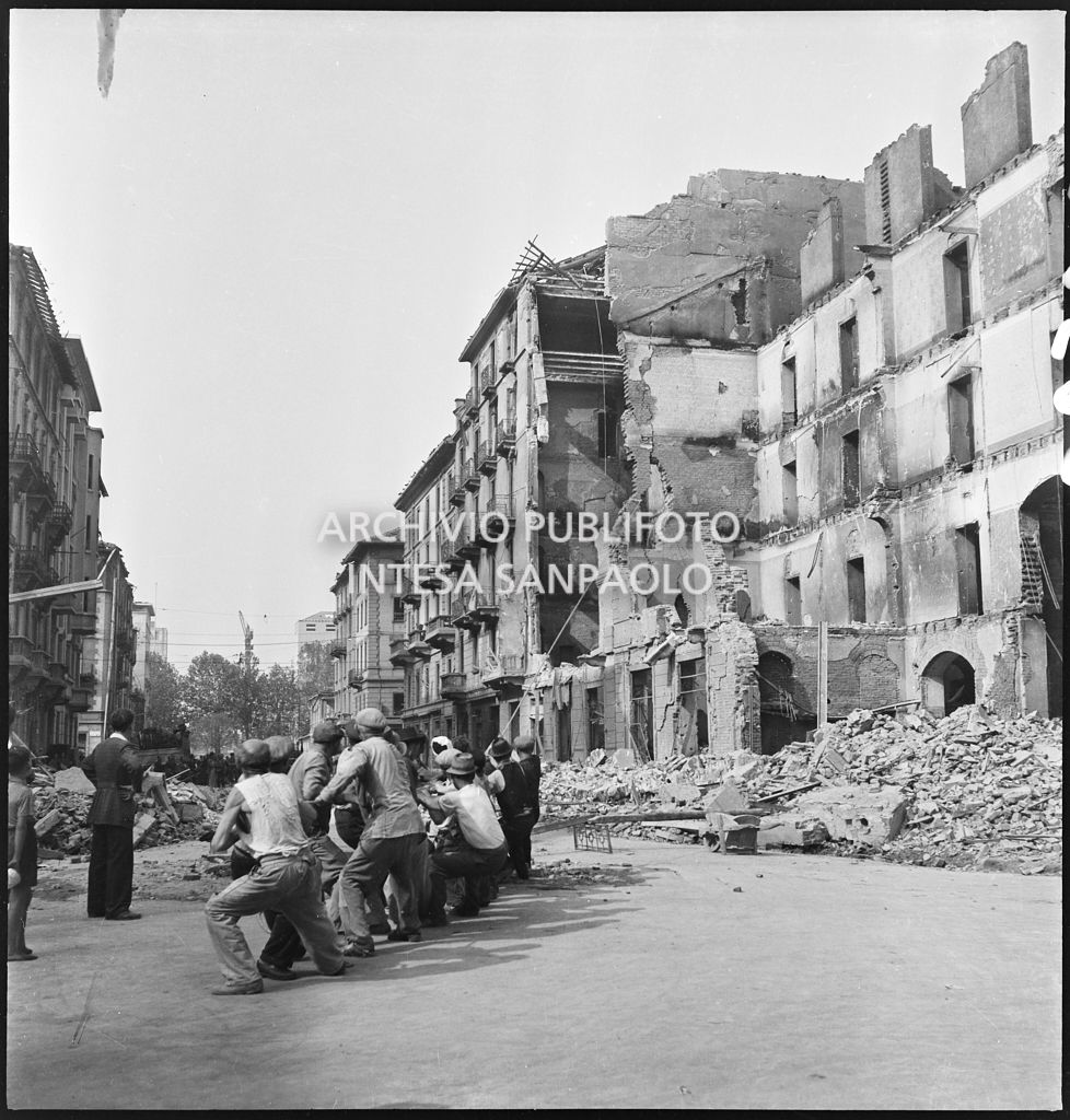 Un gruppo di uomini, per mezzo di una fune, abbatte il muro pericolante di un edificio sventrato dai bombardamenti in via Giuseppe Prina a Milano