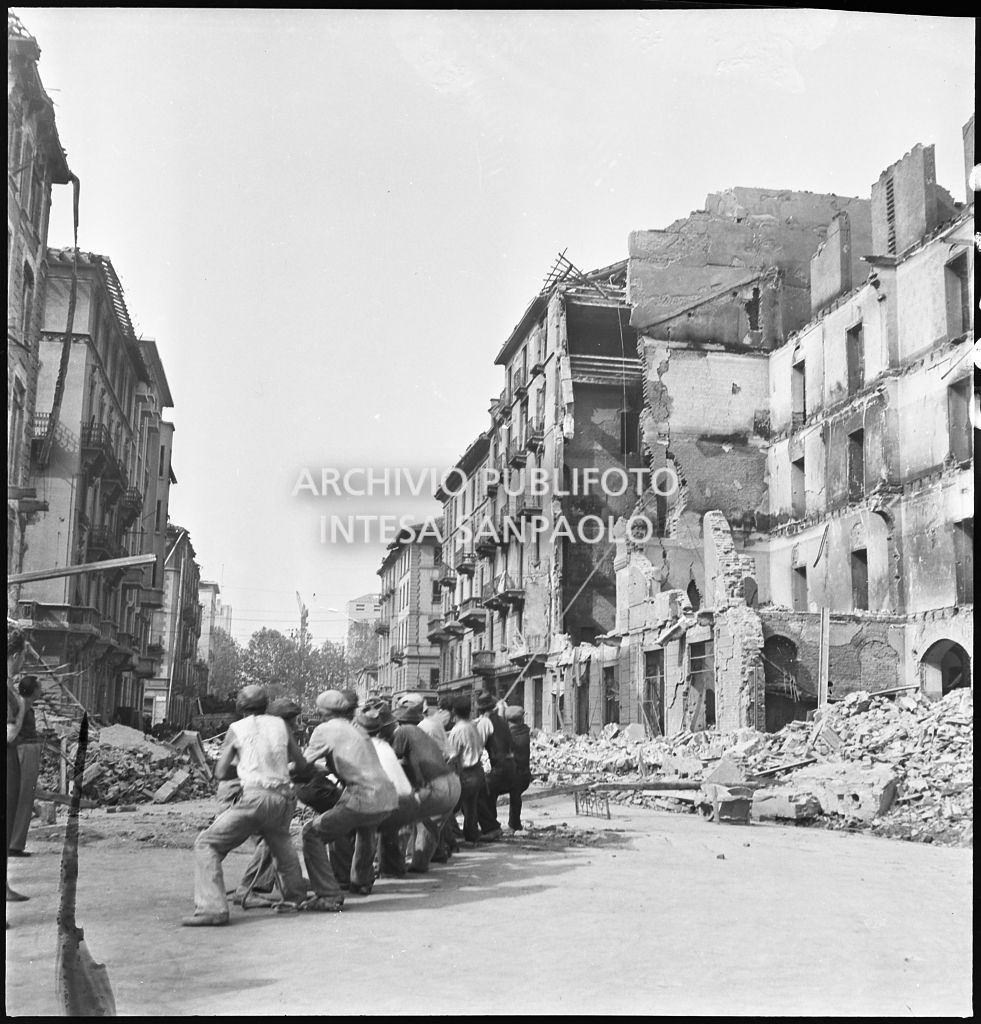 Un gruppo di uomini, per mezzo di una fune, abbatte il muro pericolante di un edificio sventrato dai bombardamenti in via Giuseppe Prina a Milano
