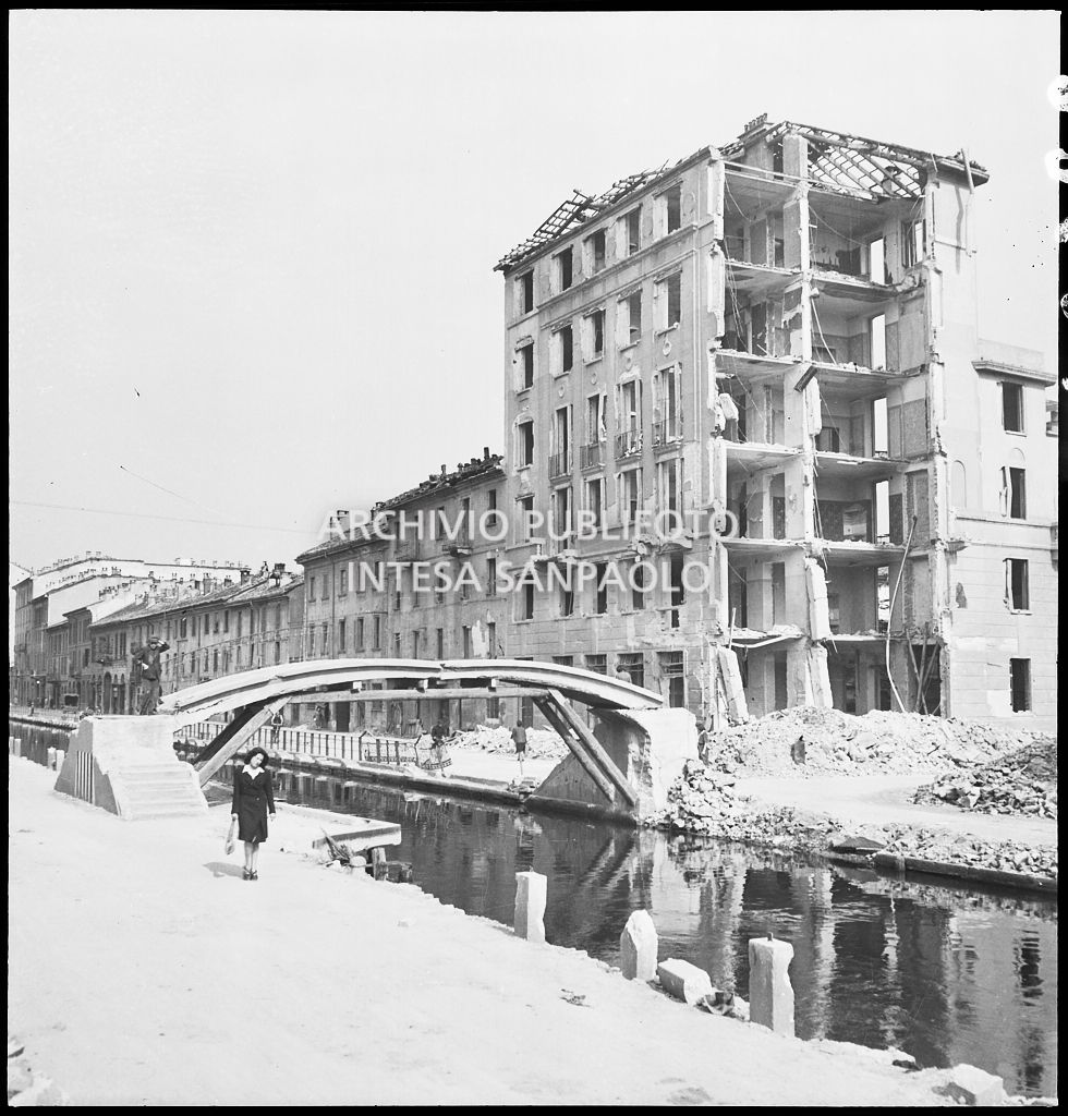 Scorcio del Naviglio Pavese su cui affaccia un edificio sventrato dai bombardamenti; il ponte pedonale è danneggiato ma ha resistito