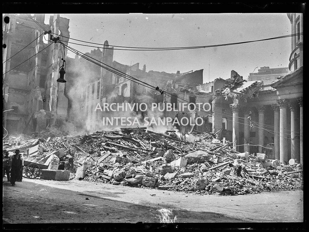 Piazza San Carlo a Milano, all'indomani dei bombardamenti, ingombra delle macerie, ancora fumanti, degli edifici e della basilica di San Carlo al Corso gravemente danneggiati durante gli attacchi aerei