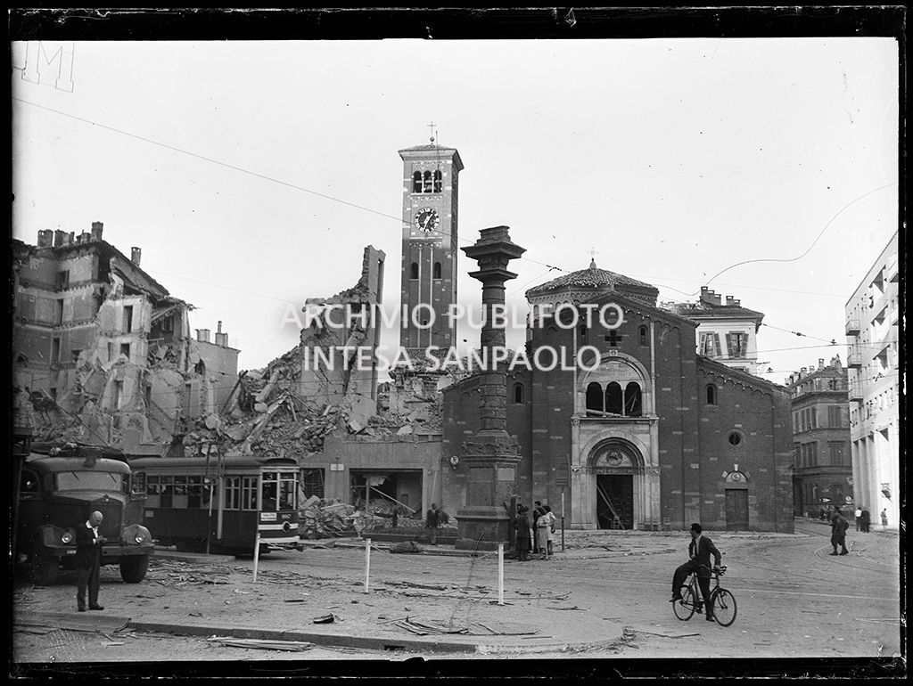 Basilica di San Babila, nell'omonimo largo (oggi piazza San Babila) a Milano, gravemente danneggiata dai bombardamenti, così come la Colonna del Leone e l'edificio all'inizio di corso Venezia, completamente distrutto. Sulla sinistra un tram tipo 1928 , linea 3 con la fasce bianche per renderlo più visibile durante l'oscuramento
