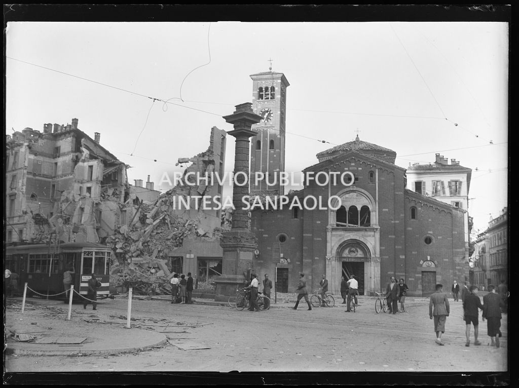 Basilica di San Babila, nell'omonimo largo (oggi piazza San Babila) a Milano, gravemente danneggiata dai bombardamenti, così come la Colonna del Leone e l'edificio all'inizio di corso Venezia, completamente distrutto. Sulla sinistra un tram tipo 1928 , linea 3 con la fasce bianche per renderlo più visibile durante l'oscuramento
