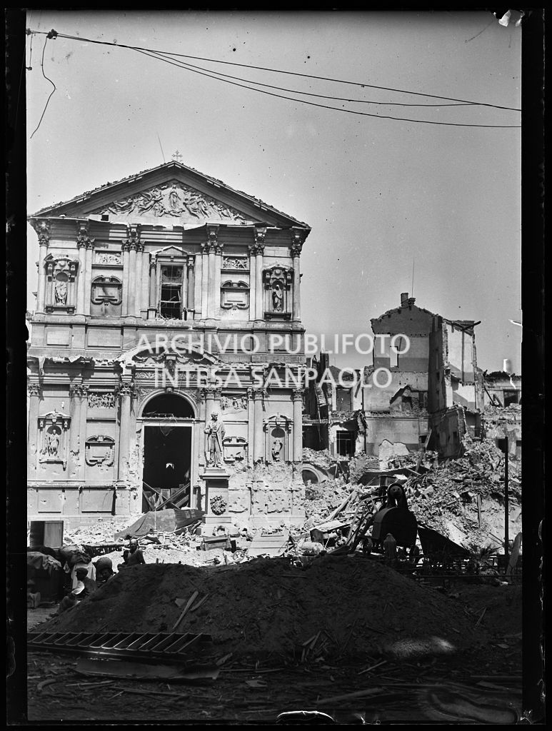 Chiesa di San Fedele, nell'omonima piazza a Milano, gravemente danneggiata dai bombardamenti; sulla destra l'edificio che ospitava la questura della città, completamente distrutto; davanti alla chiesa il monumento a Alessandro Manzoni intatto.