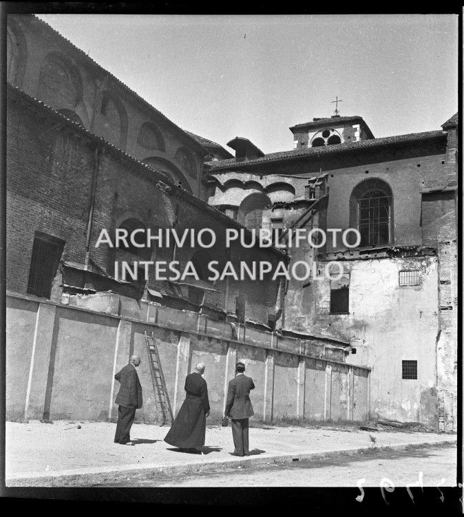 Un religioso e due uomini osservano i danni dei bombardamenti alla basilica di San Simpliciano a Milano