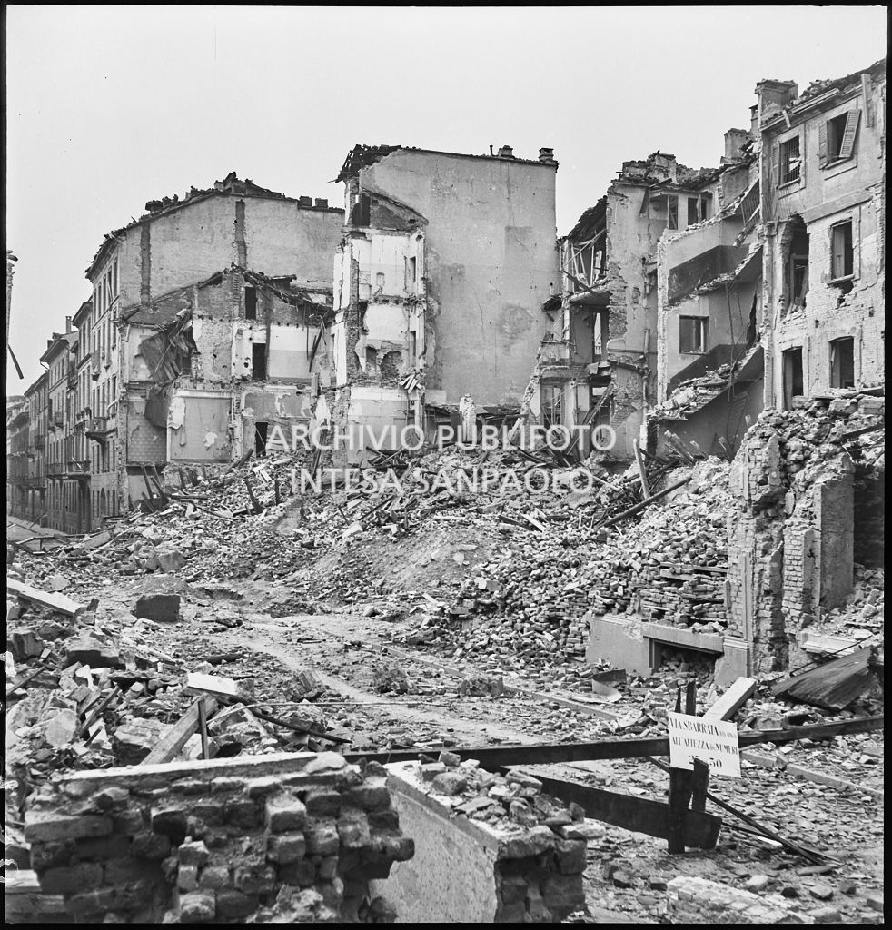 Edifici distrutti dai bombardamenti in via Santo Spirito a Milano. Sulla sbarra il cartello: "via sbarrata (via Spiga) all'altezza dei numeri 25 e 30"