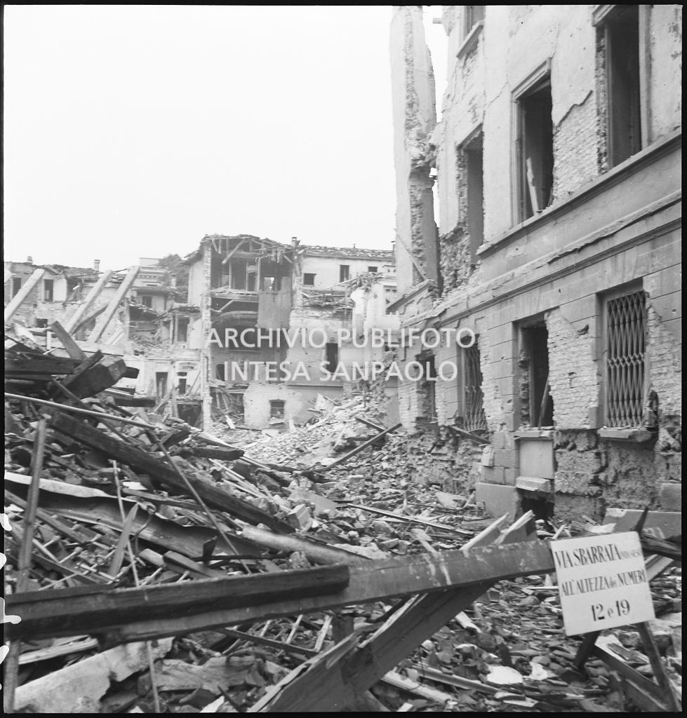 Edifici distrutti dai bombardamenti in via Gesù a Milano. Sulla sbarra il cartello: "via sbarrata (via Gesù) all'altezza dei numeri 12 e 19"