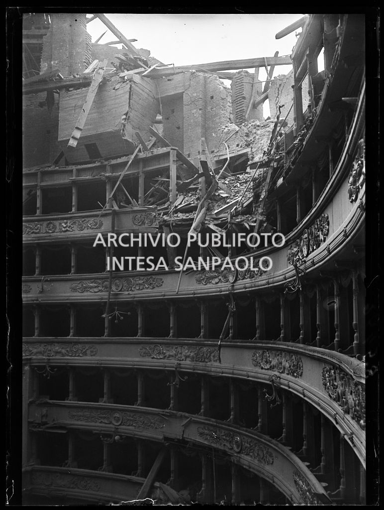 Interno del Teatro alla Scala di Milano dopo i bombardamenti: il tetto e la volta centinata sottostante sono completamente crollati distruggendo in parte il quinto e sesto ordine di gallerie e danneggiando i palchi, il proscenio e la platea
