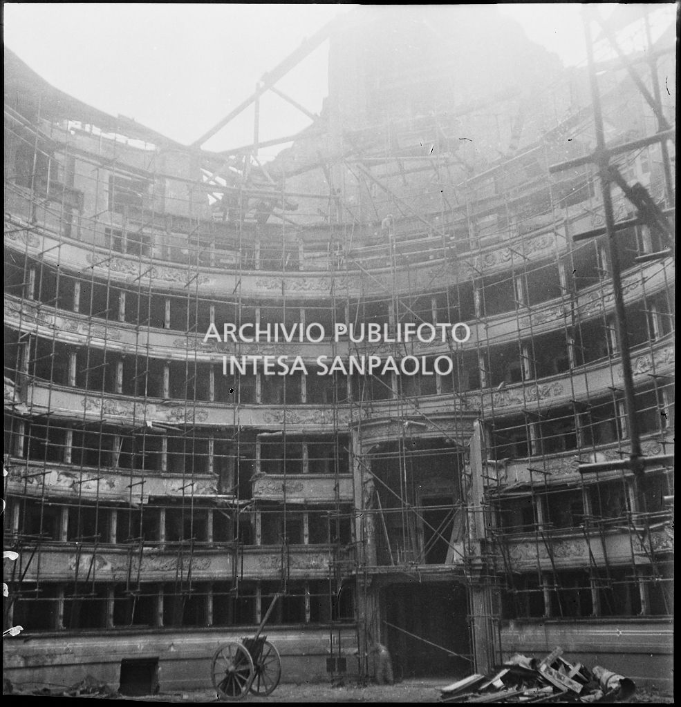 Scorcio dell'interno del Teatro alla Scala di Milano gravemente danneggiato dai bombardamenti e immediatamente messo in sicurezza con una struttura di tubi metallici, dopo aver rimosso le macerie. A destra il palco reale