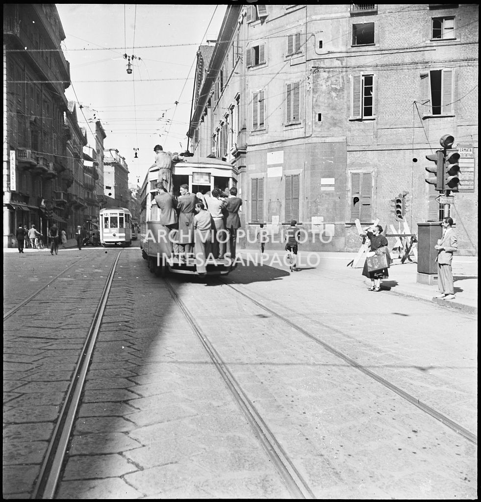 Tram tipo 1928 in transito in corso Venezia a Milano nei giorni dei bombardamenti della città; la vettura è così affollata che alcuni passeggeri viaggiano in piedi sul paraurti posteriore, sul gancio e uno si è addirittura arrampicato sul finestrino. Sullo sfondo si intravede Palazzo Serbelloni