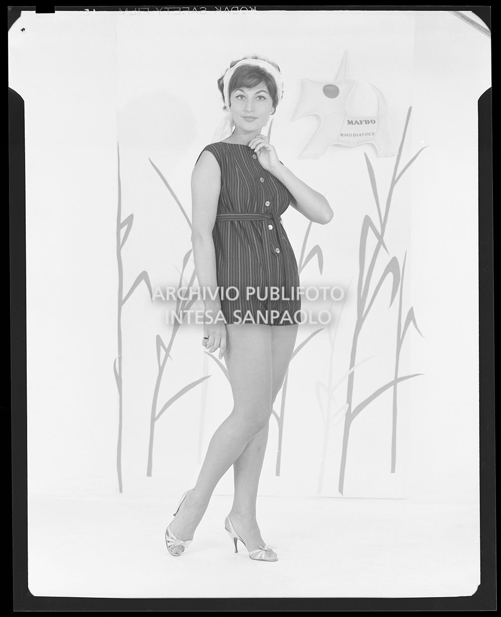 Indossatrice con costume intero a righe con cintura in vita. Sullo sfondo si vede il logo: un cane con una pettorina che riporta la scritta "Mafbo Rhodiatoce"<br>21210