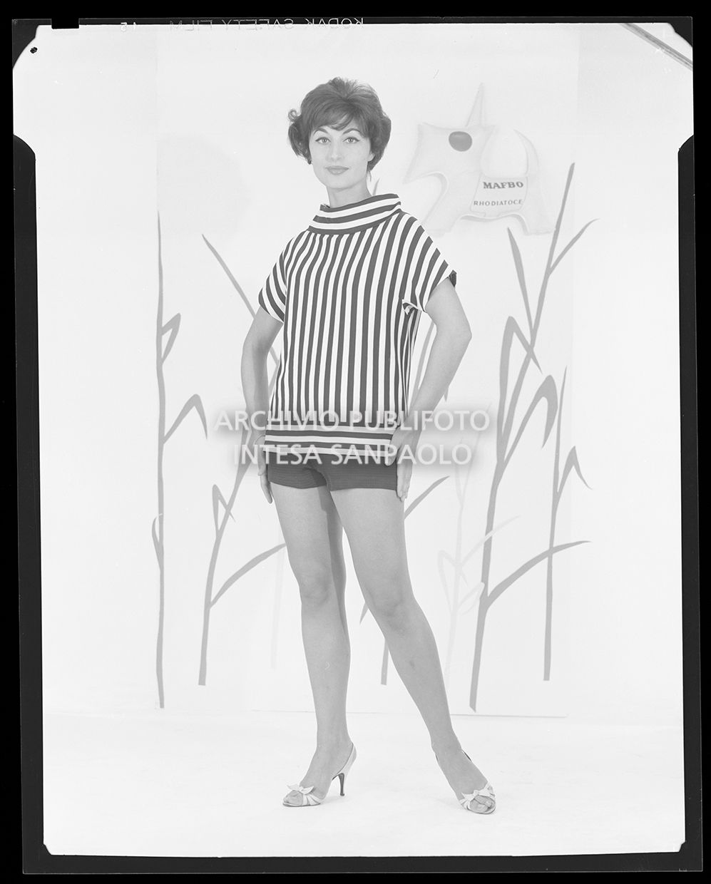 Indossatrice con maglietta a righe e pantaloncini. Sullo sfondo si vede il logo: un cane con una pettorina che riporta la scritta "Mafbo Rhodiatoce"<br>21212