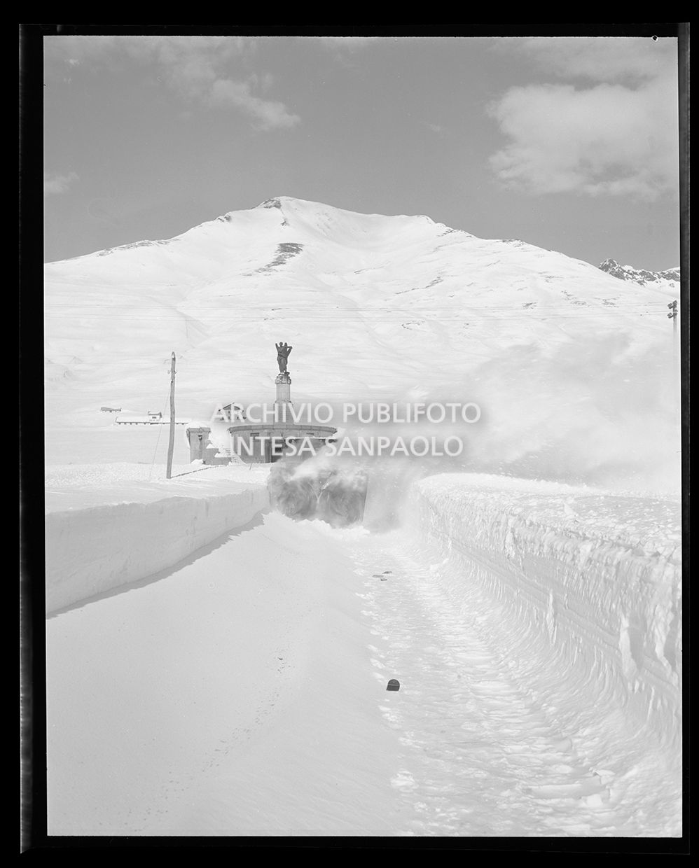 Spazzaneve in funzione su una strada con alle spalle il sacrario militare del Tonale<br>25241
