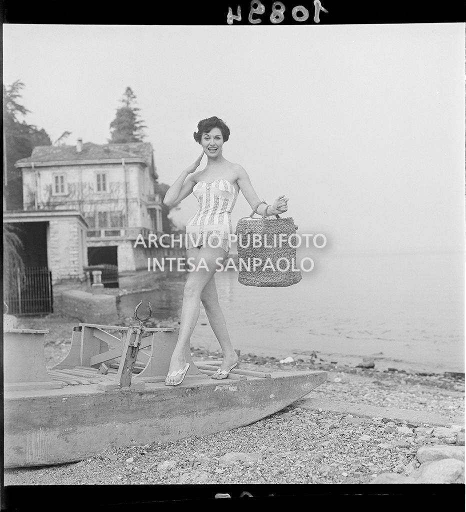 Indossatrice con costume da bagno intero a righe e borsa in paglia sulla spiaggia<br>10894