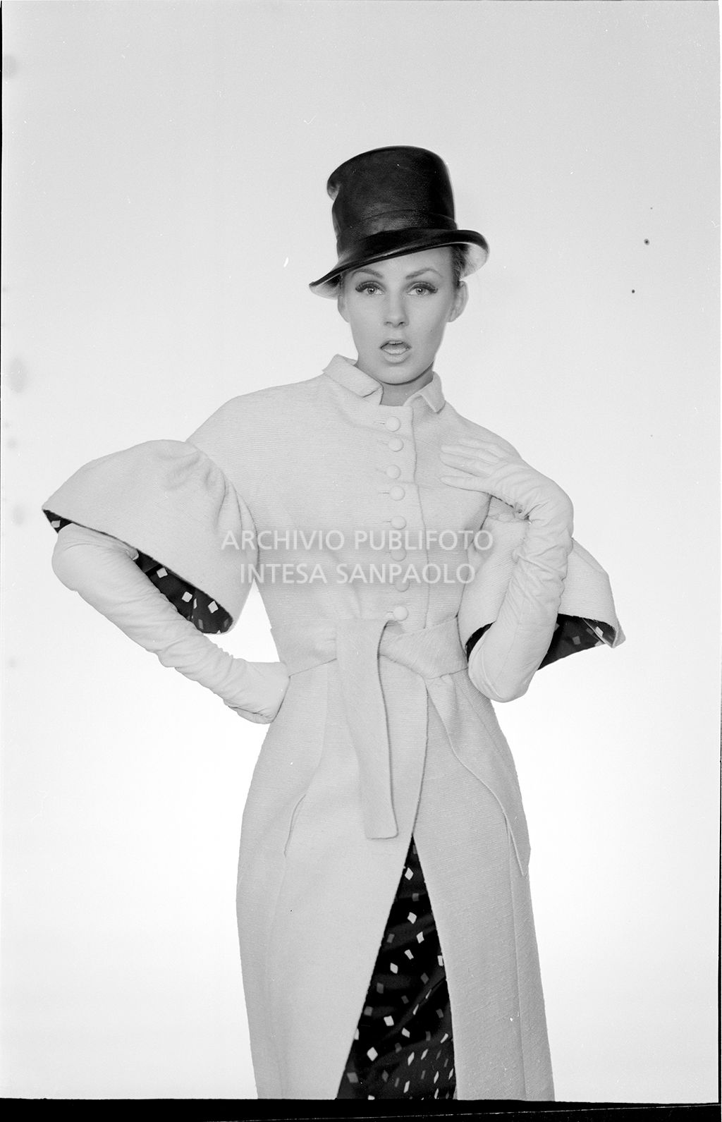 Indossatrice con cappotto legato in vita, maniche a sbuffo, guanti e cappello<br>10914