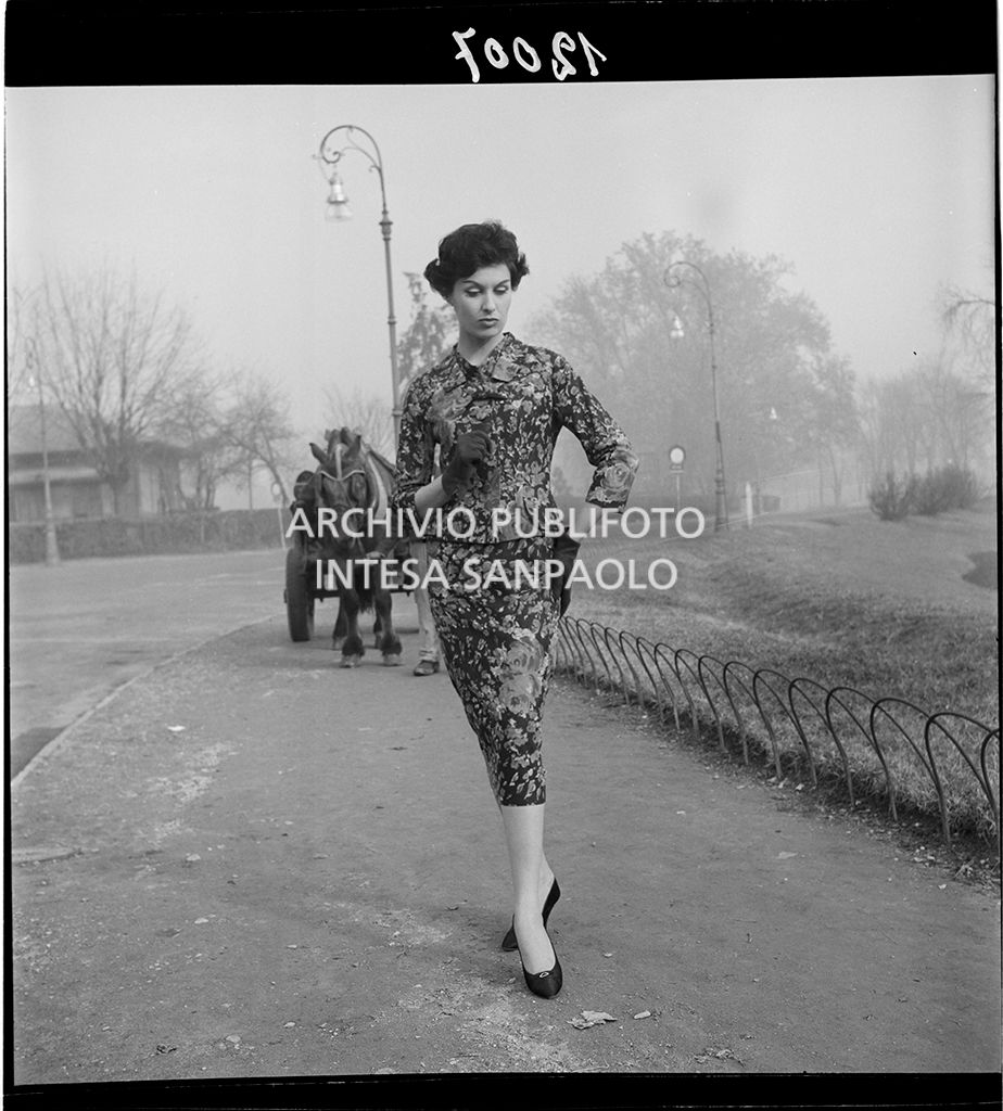 Indossatrice con tailleur fiorato e guanti. Sullo sfondo un carretto trainato da un cavallo<br>12007