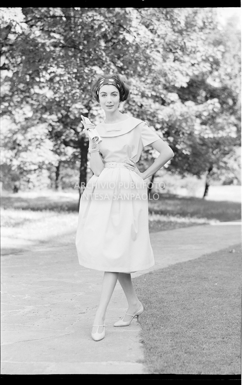 Indossatrice con abito, guanti e fascia sui capelli in un parco<br>18601