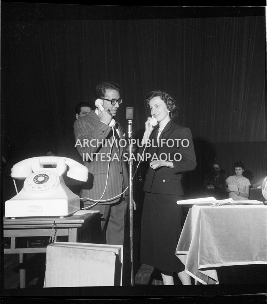 Mike Bongiorno con una donna al telefono di fronte ad un microfono<br>18743