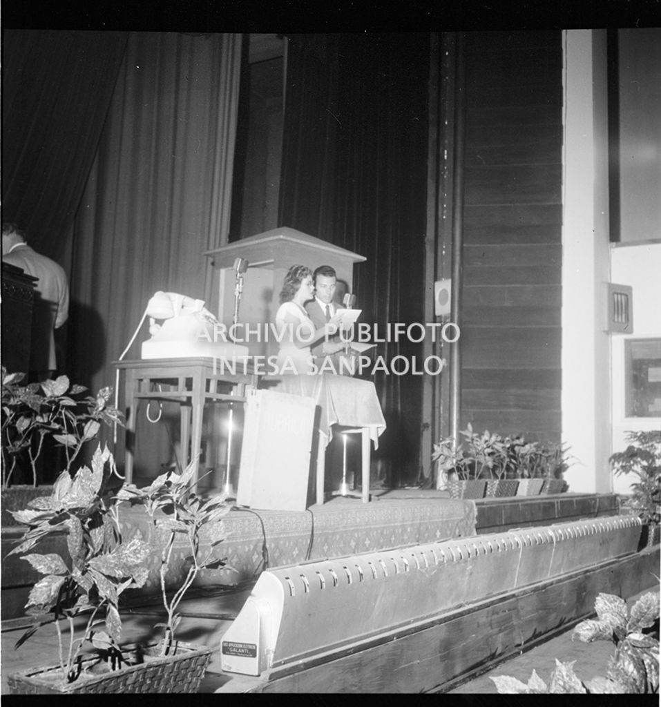 Mike Bongiorno con una donna di fronte ad un microfono<br>18749