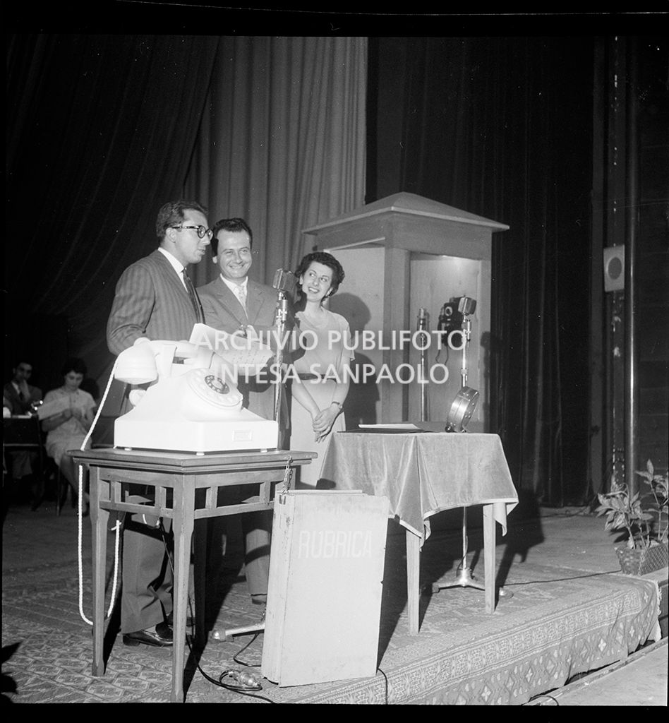 Mike Bongiorno con una donna  ed un uomo di fronte ad un microfono<br>18758