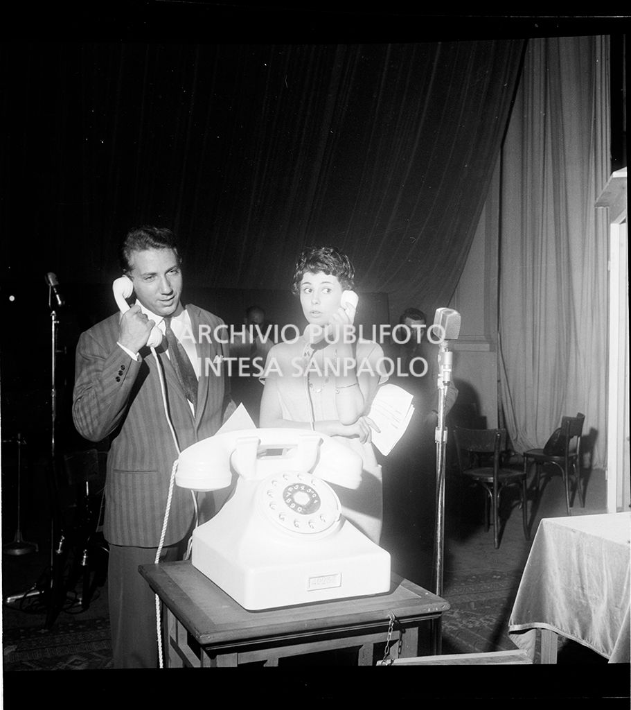 Mike Bongiorno con una donna al telefono di fronte ad un microfono<br>18765