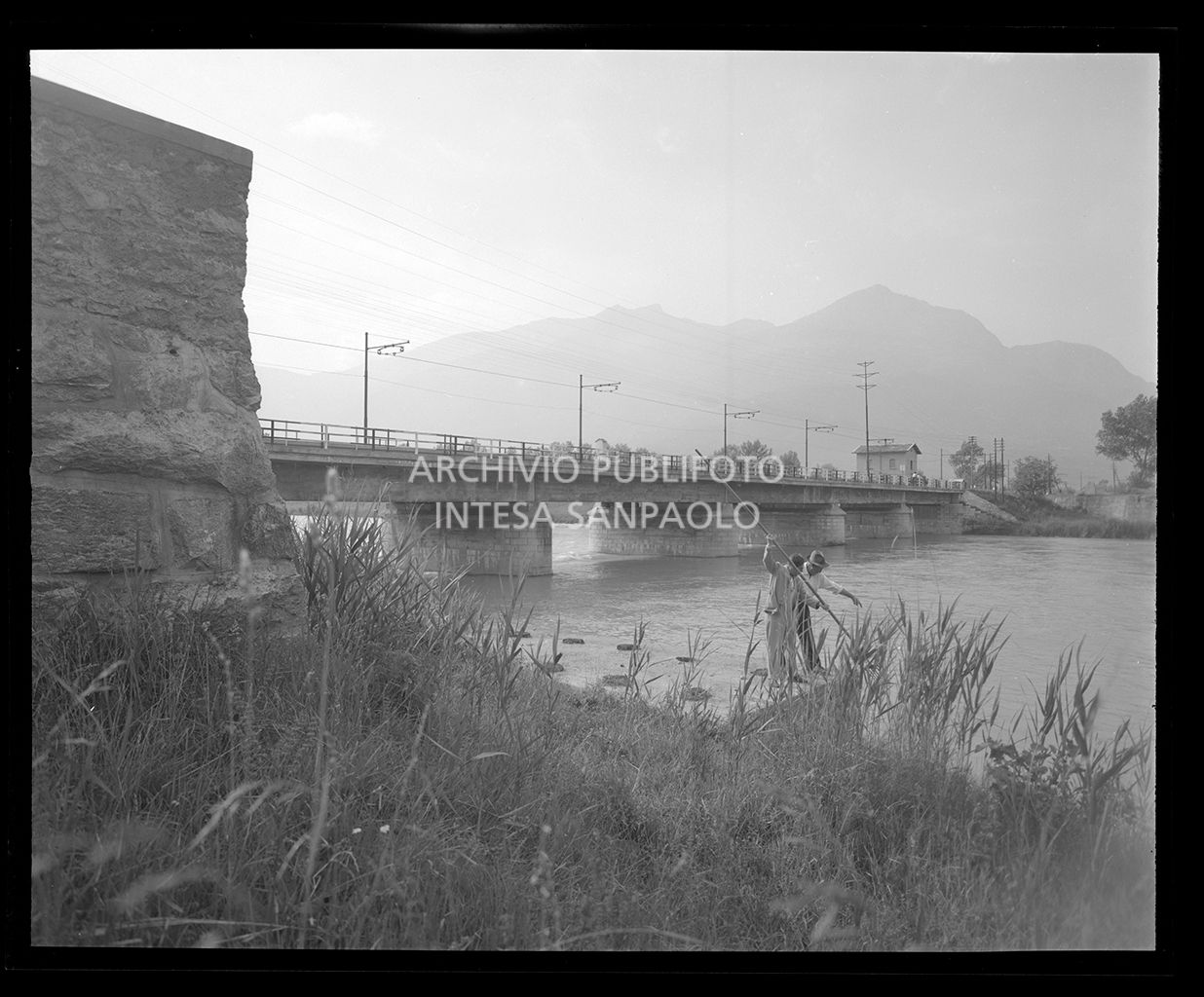 Ponte su un fiume con due uomini sull'argine che lo puliscono con un rastrello (simile agli scatti 19308, 19315, 19316, 19317, 19319)<br>19305