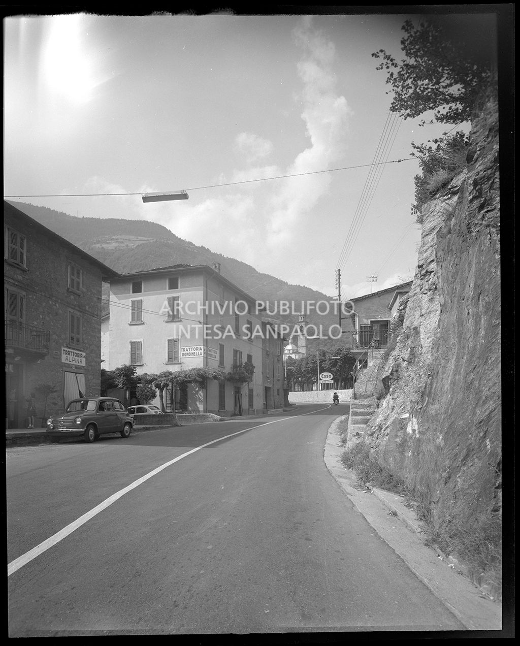 Strada di Edolo con la Trattoria Alpina e la Trattoria Rondinella e sullo sfondo si vele la cupola e il campanile della chiesa Arcipretale<br>19599