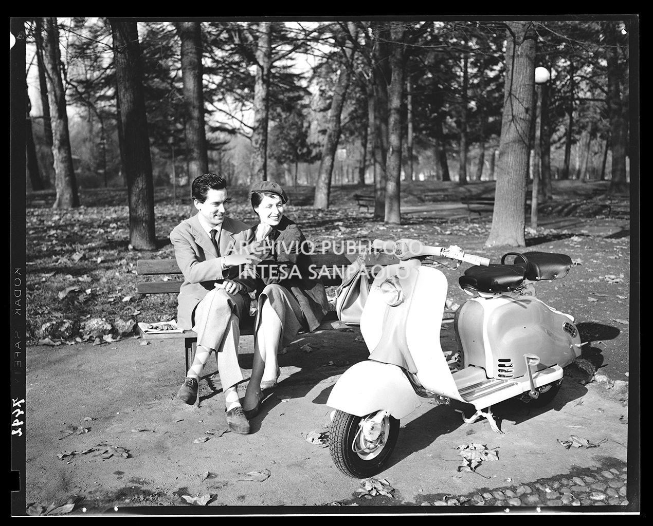 Uomo e donna seduti su una panchina nel parco che osservano la Lambretta<br>7392