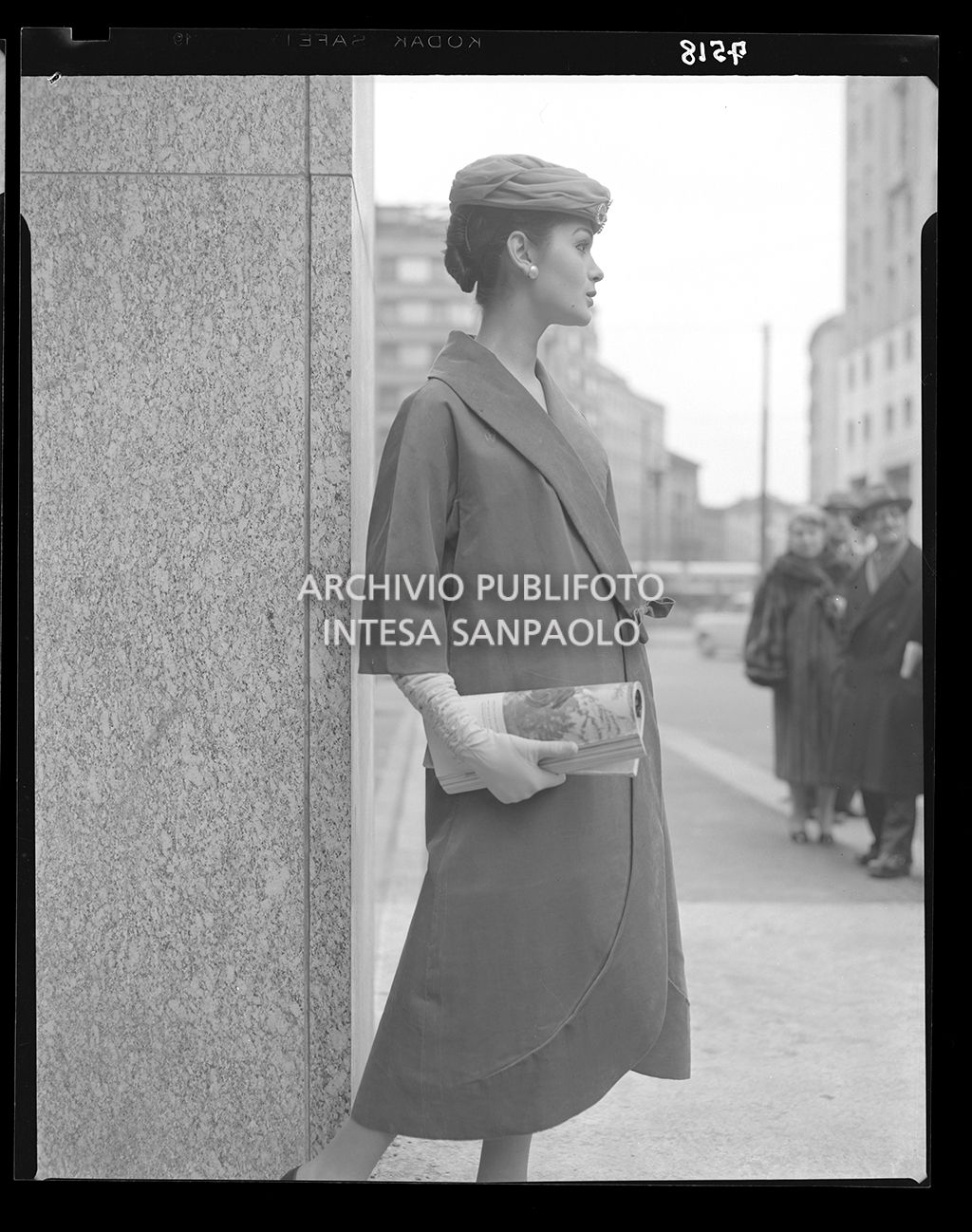 Donna con soprabito, guanti e cappello; tiene in mano una rivista<br>7518