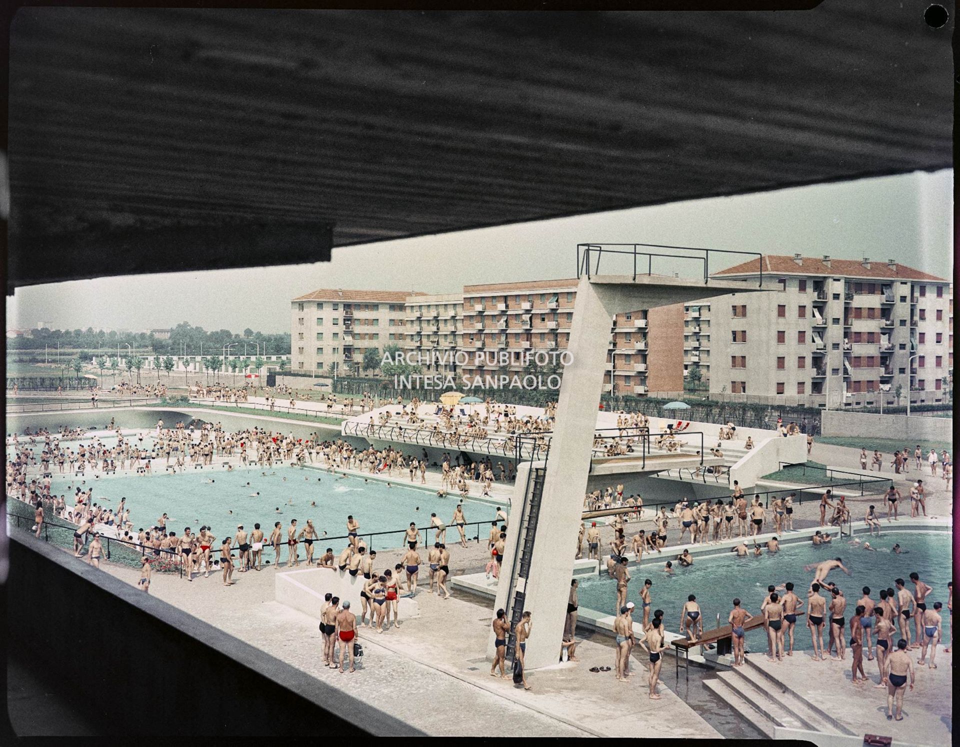 Piscine con bagnanti viste dall'alto. In primo piano una serie di trampolini, mentre sullo sfondo sono visibili dei palazzi<br>1589