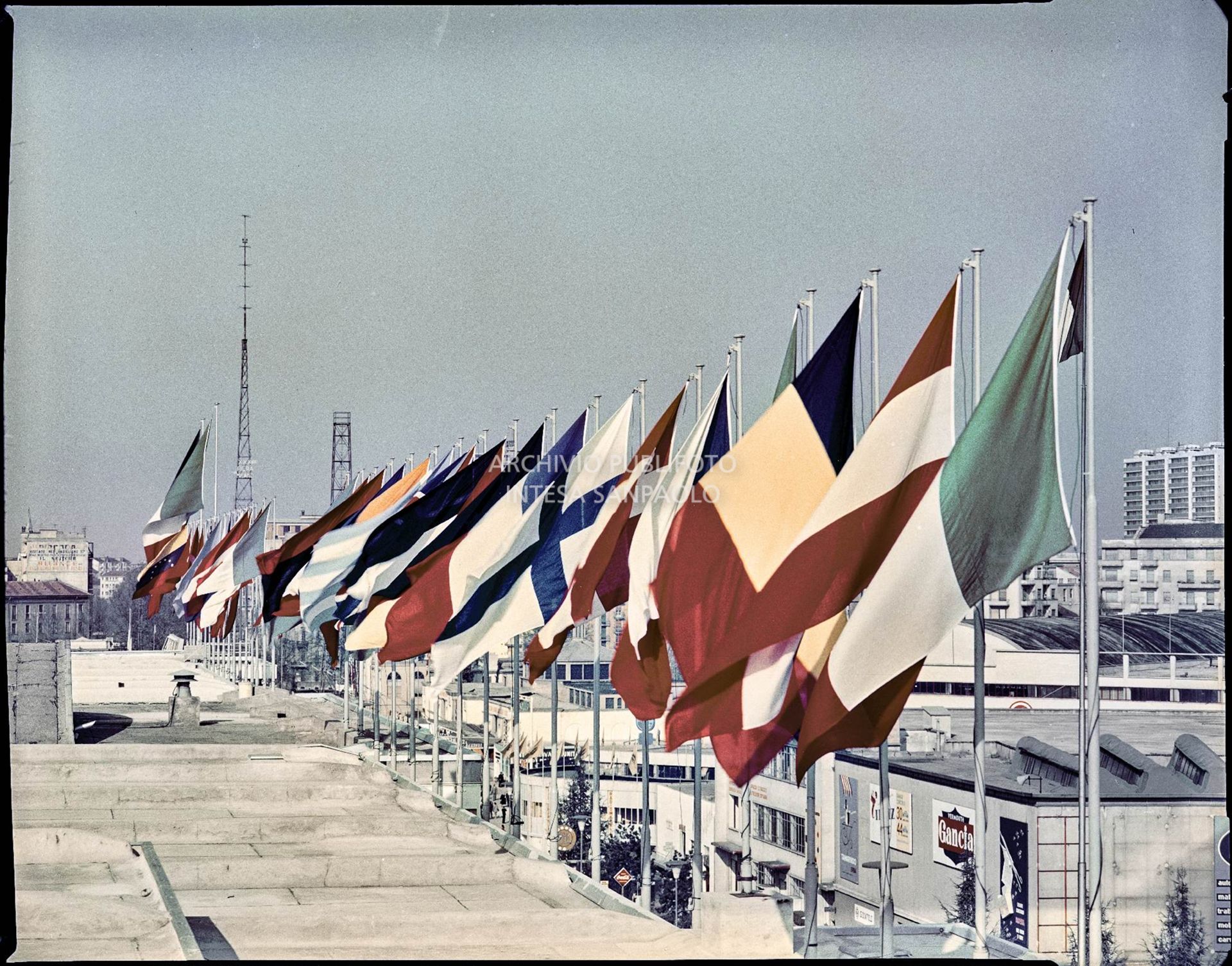 Bandiere al vento sul tetto del Palazzo delle Nazioni e vista su viale dell'industria alla Fiera Campionaria del 1960<br>3033