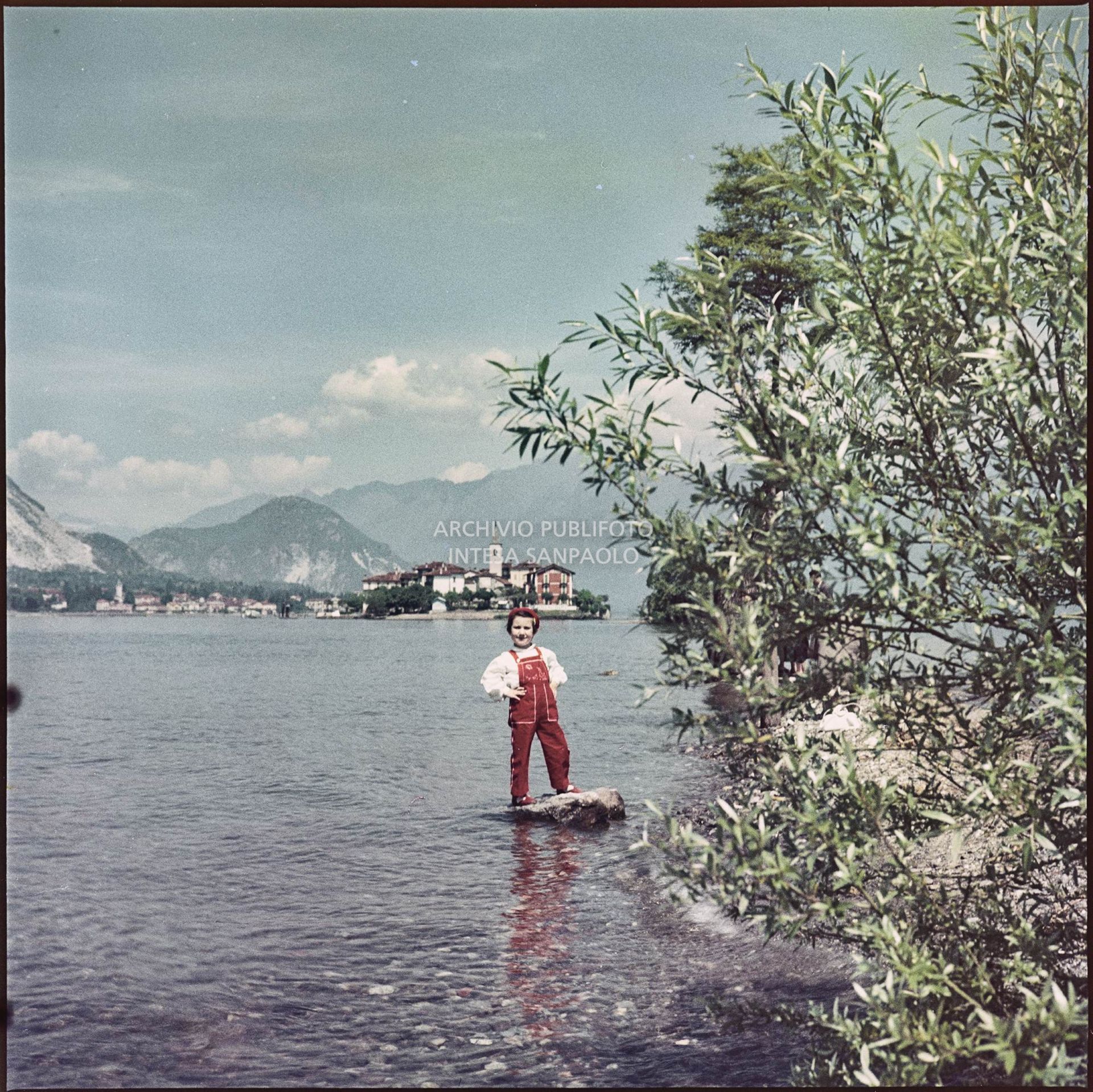 Bambina in posa su uno scoglio in riva al lago Maggiore. Sullo sfondo è visibile l'Isola dei Pescatori<br>347