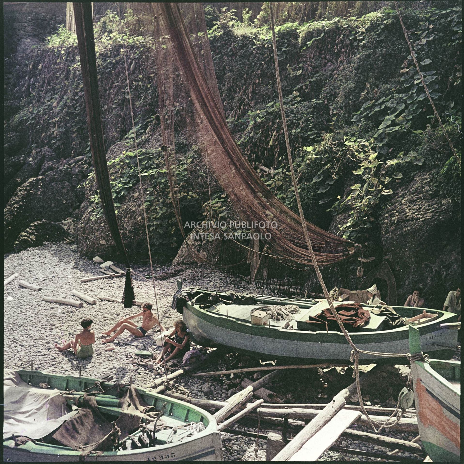 Bagnanti sulla spiaggia di Portofino accanto ad imbarcazioni in legno e reti da pesca<br>4932