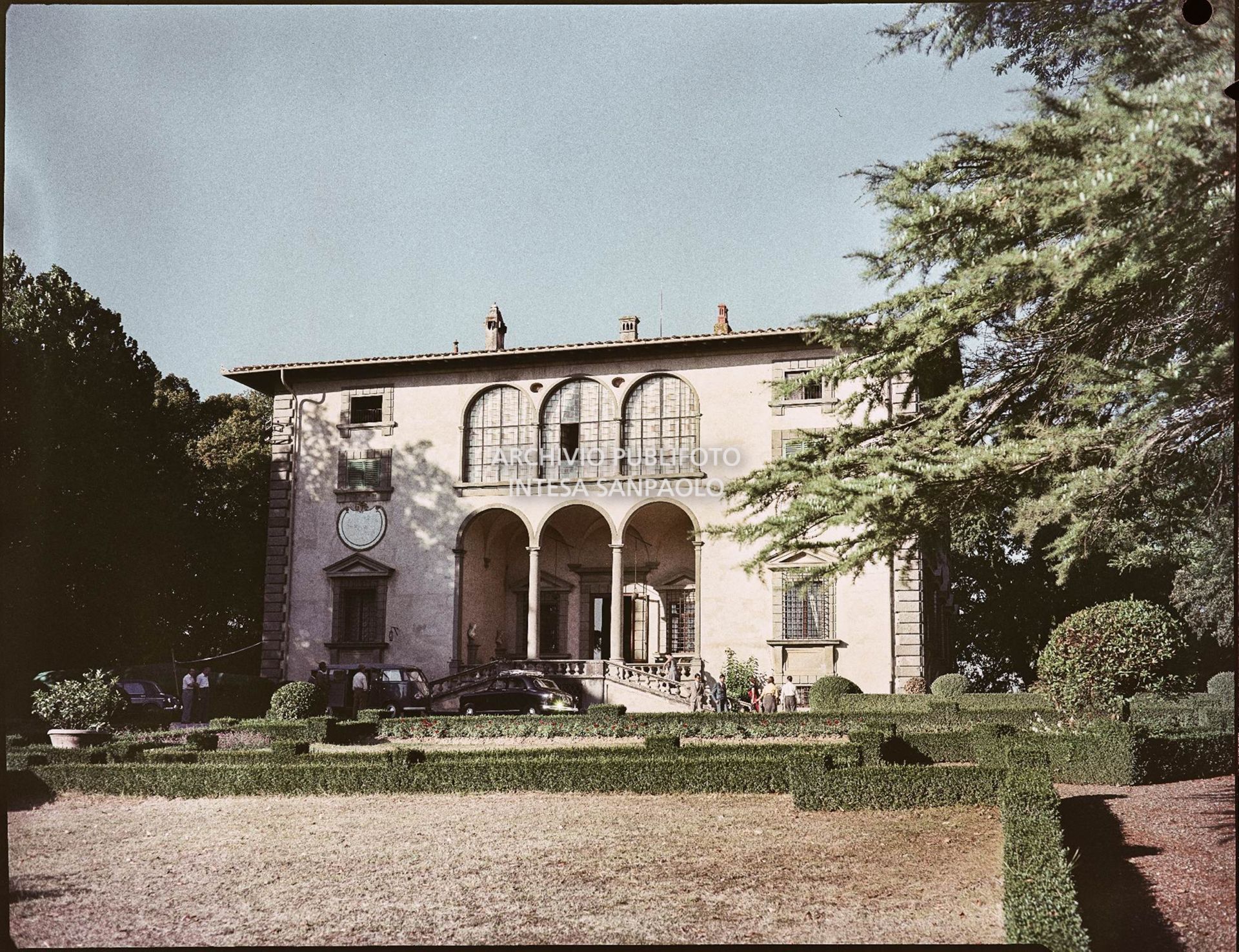 Veduta esterna della villa e del giardino; visibili alcune persone ed automobili parcheggiate<br>820