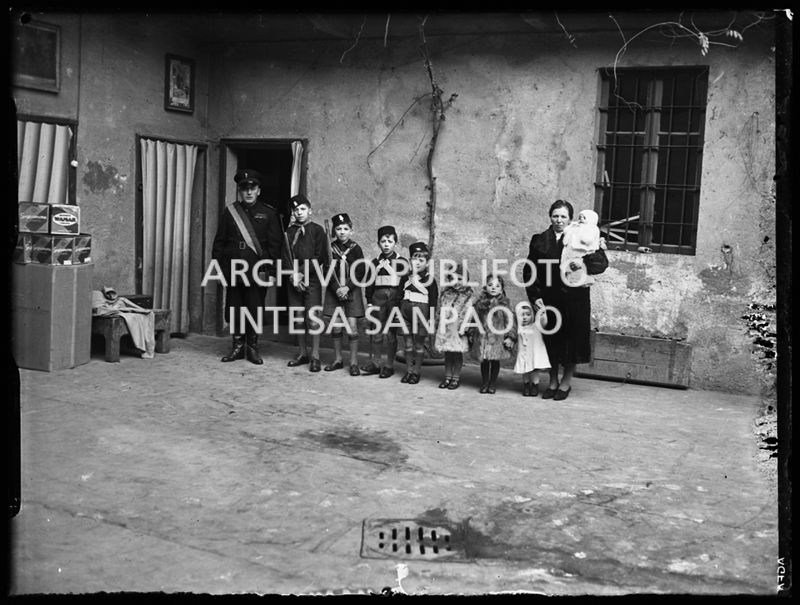 Una coppia, con i suoi otto figli, ritratta davanti all'entrata di casa; i figli maschi indossano divise da balilla e due di loro imbracciano il moschetto