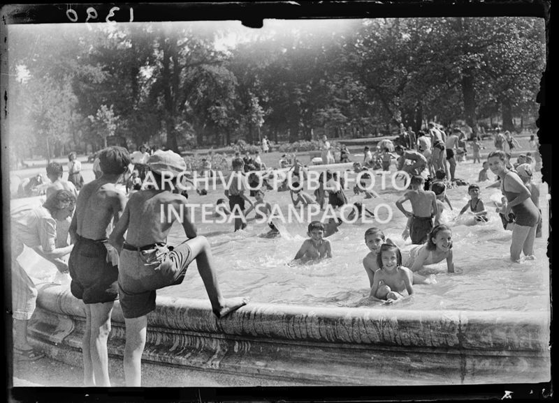 Due ragazzini osservano la fontana dei Giardini Pubblici di Milano utilizzata come piscina dai bambini in occasione di un'eccezionale ondata di caldo estivo