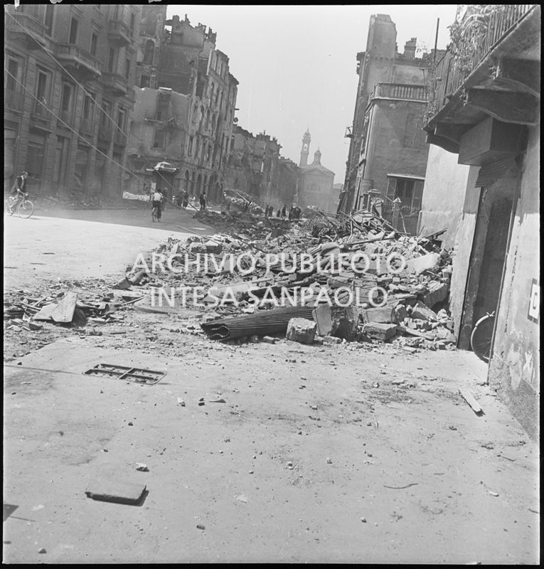 Scorcio di via Molino delle Armi a Milano con gli edifici distrutti dai bombardamenti. In primo piano macerie addossate ai lati della strada per consentire la circolazione nella via. Sullo sfondo la chiesa di Santa Maria della Vittoria