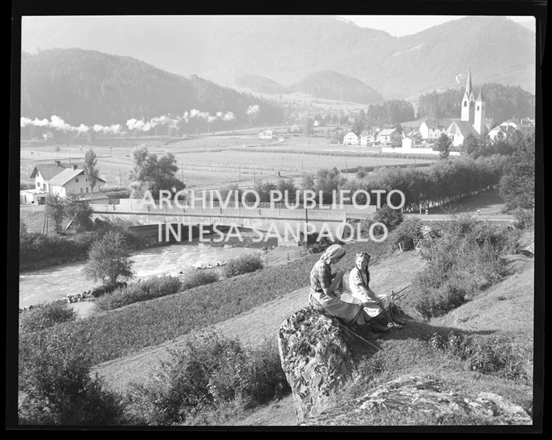 Una donna ed una bambina sedute su una roccia ed in lontananza un ponte e delle case<br>29867