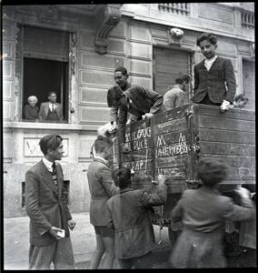 Un gruppo di bambini scrive con il gesso sul cassone di un camion, visibili le scritte "[w rovesciata] la Repubblica", "[w rovesciata] il duce"