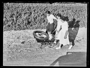 Una donna spinge un bambino in carrozzina, in compagnia di altre due donne, lungo una strada di campagna